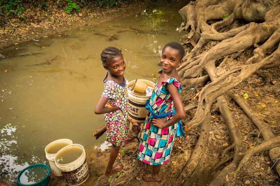 Two girls fetch water with buckets from a dirty river