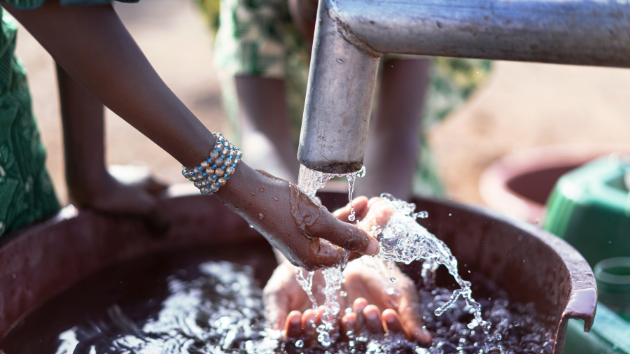 Hands catching water flowing from a spout into a bucket