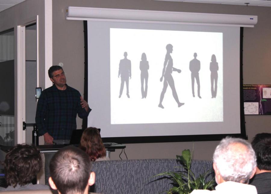Gregory Bratman presenting in front of a group while standing in front of a screen with five human figures on it