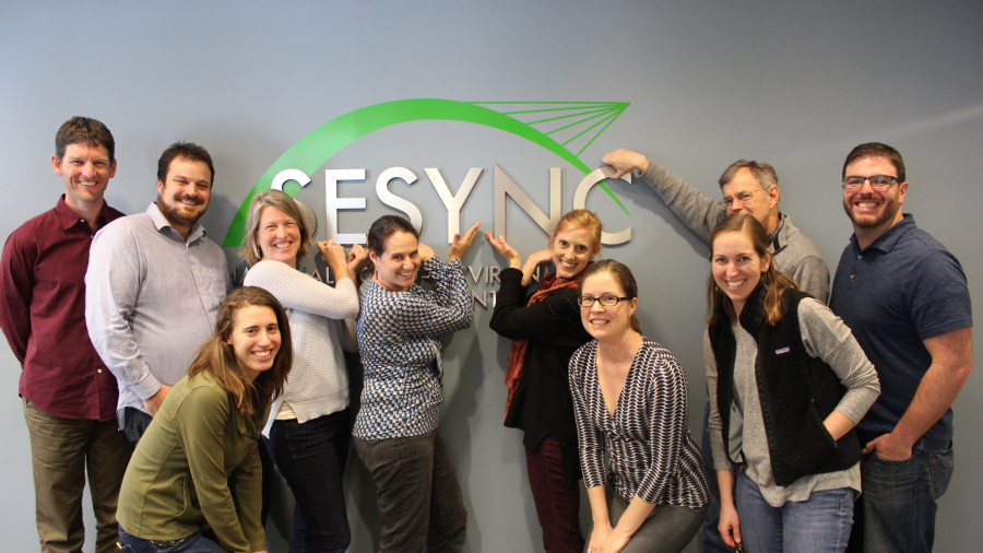 A team pointing to the SESYNC sign behind them