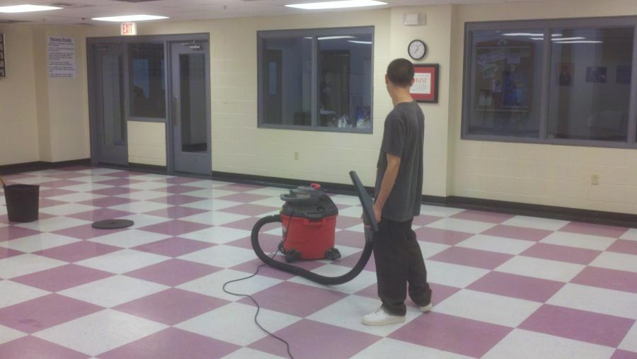 A man with his back to the camera cleaning a classroom floor