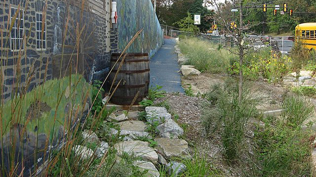 A rain barrel standing outside the wall of a building 