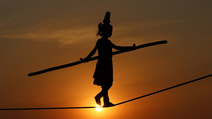 The silhouette of a young girl walking across a tightrope in front of a sunset with the sun low in the orange sky