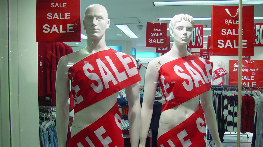 Two mannequins draped in sale banners inside a store window with more sale signs behind them