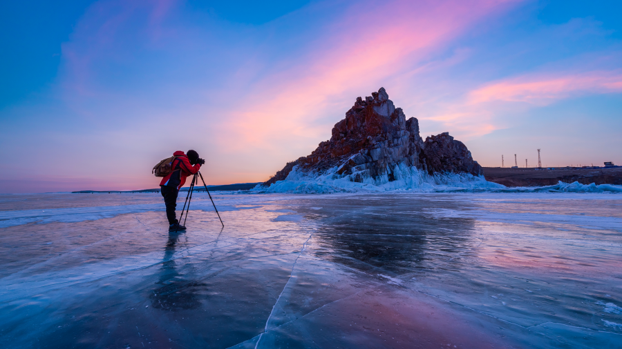 A person taking a photograph of the landscape with a camera set up on a tripod on a frozen lake