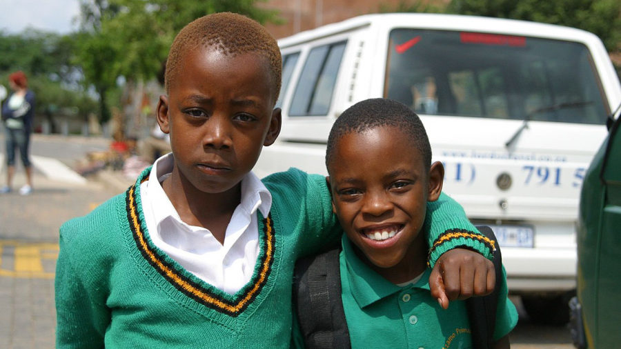 Two school-aged children in their school uniforms with one child putting his arm around the other