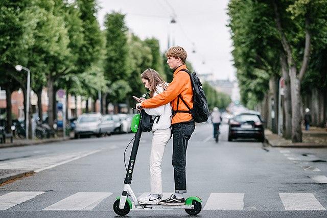Two young people riding on a motorized scooter in a crosswalk on a road