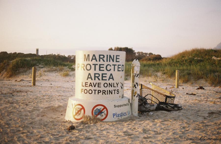A sign saying "Marine Protected Area: Leave only footprints." on a beach next to plastic debris.