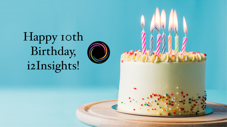 A white birthday cake with lit candles against a blue backdrop with the text "Happy 10th Birthday, i2Insights!"