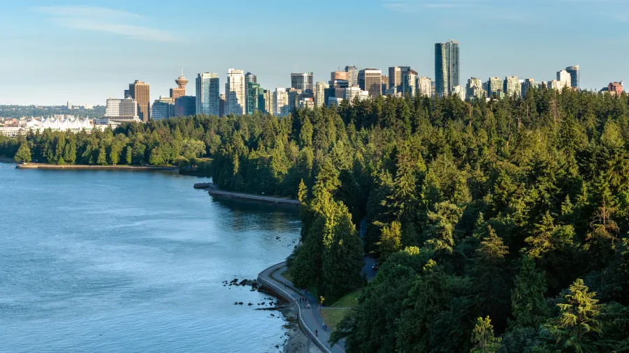 A forest along a shoreline in the foreground with the Vancouver skyline in the background