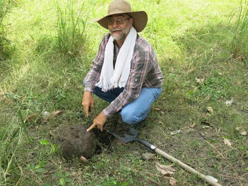 A man kneeling on the ground pointing at a mound of dirt