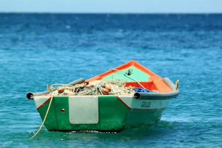 An empty fishing boat filled with gear sitting on top of bright blue water