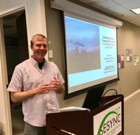 Matt Huber presenting behind a SESYNC podium in front of a screen