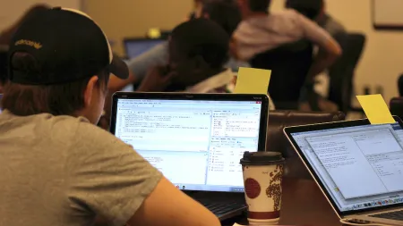 A man sitting with his back to the camera looking at code on a laptop screen