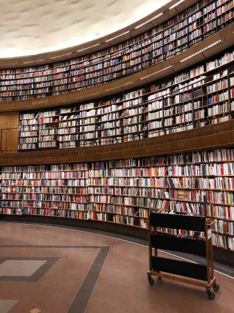 Shelves of books in a library with a rolling cart in front