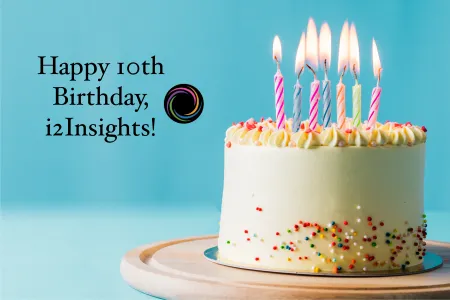 A white birthday cake with lit candles against a blue backdrop with the text "Happy 10th Birthday, i2Insights!"