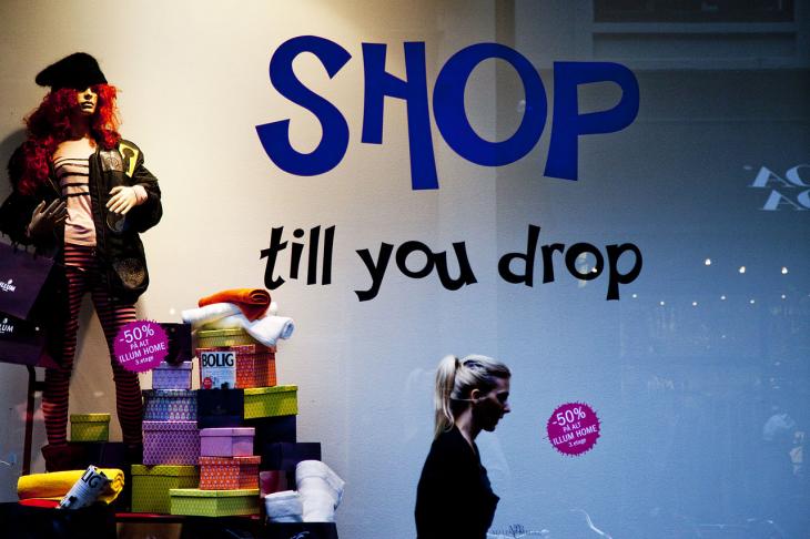 A woman walking past a store window that says "Shop till you drop"