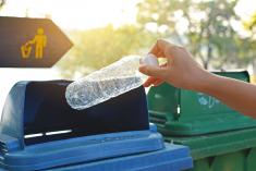 A hand holding an empty water bottle choosing between a trash or recycling bin