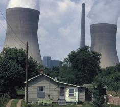 A photo of two billowing smokestacks positioned behind a small house. 